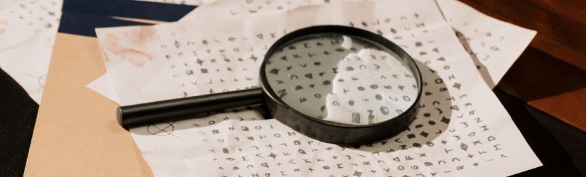 A magnifying glass on a desk with sheets of paper containing cryptic symbols